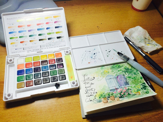 A wooden table topped with a white box filled with watercolors