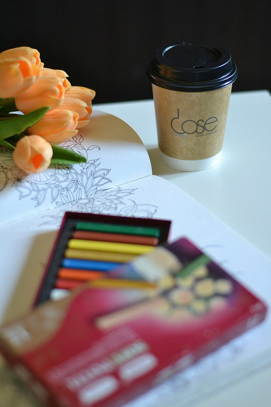 A cup of coffee sitting next to a stack of colored pencils