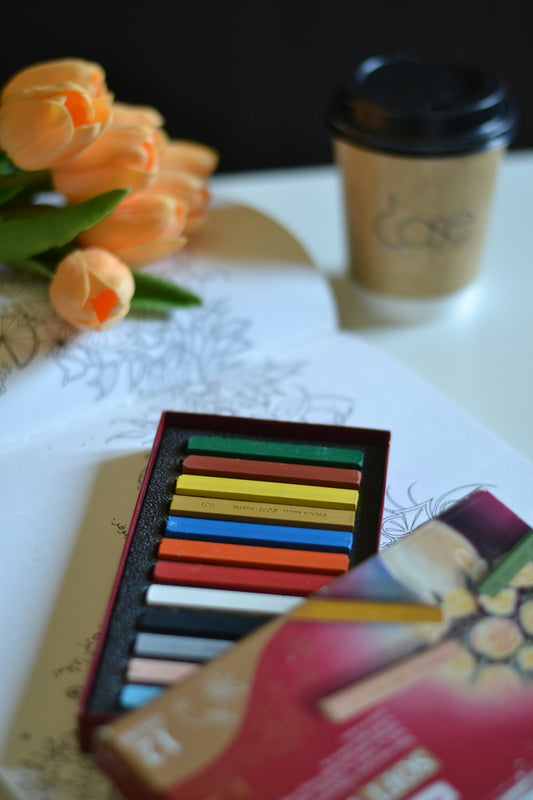 A box of colored pencils next to a cup of coffee