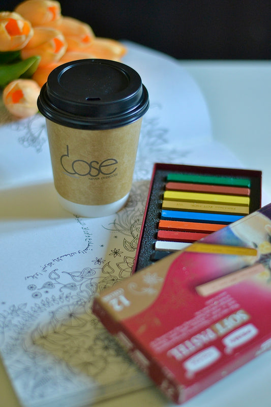 A cup of coffee next to a box of colored pencils