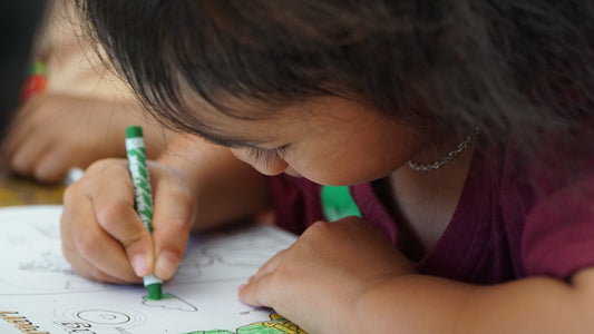 A child is coloring with a green crayon.