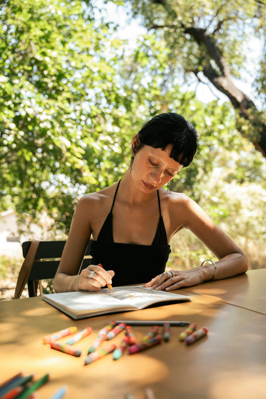 Woman drawing in a sketchbook outdoors with crayons