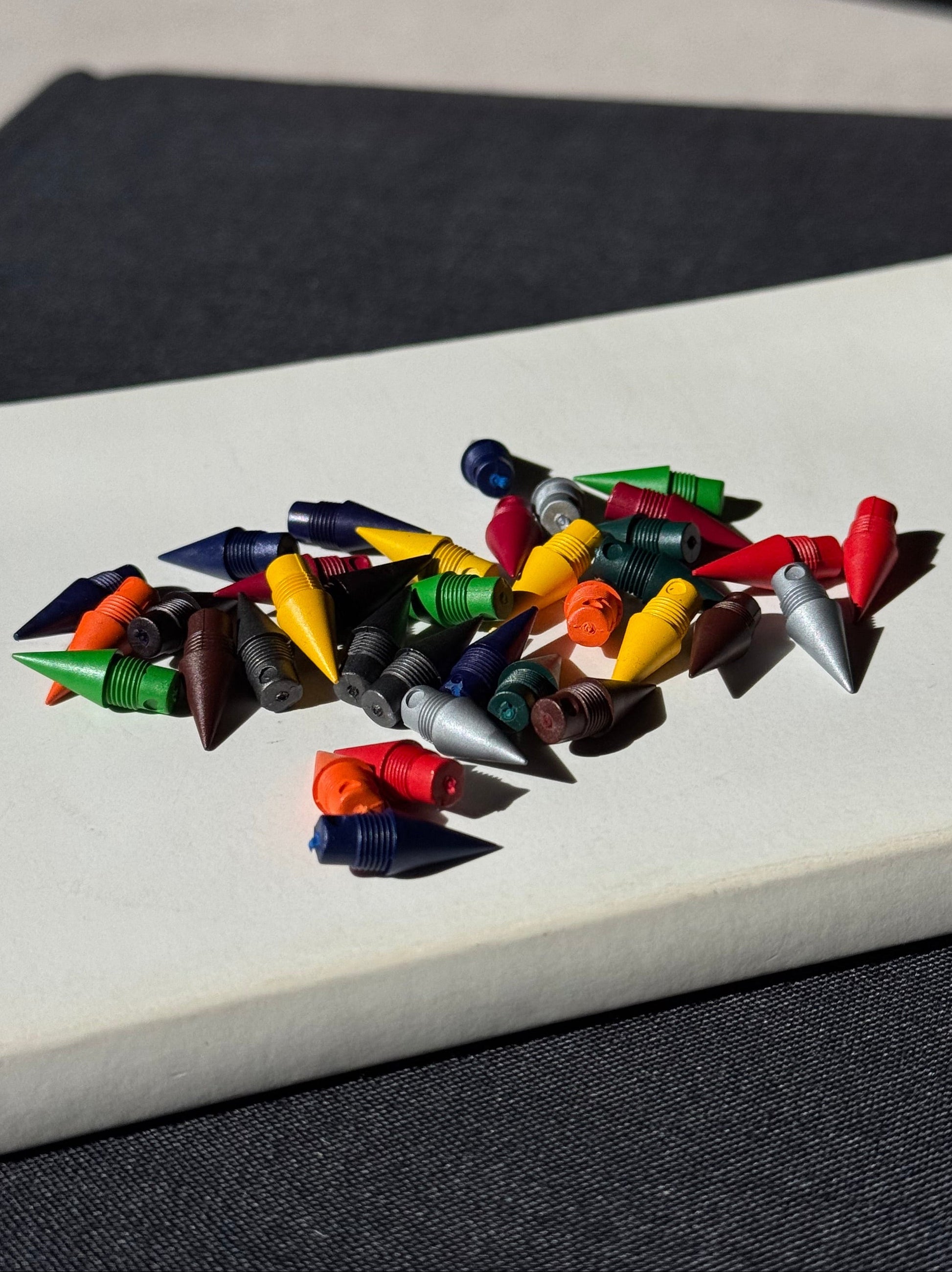 Color pencil nibs on a white book which is on a black book on a light gray surface with a black background